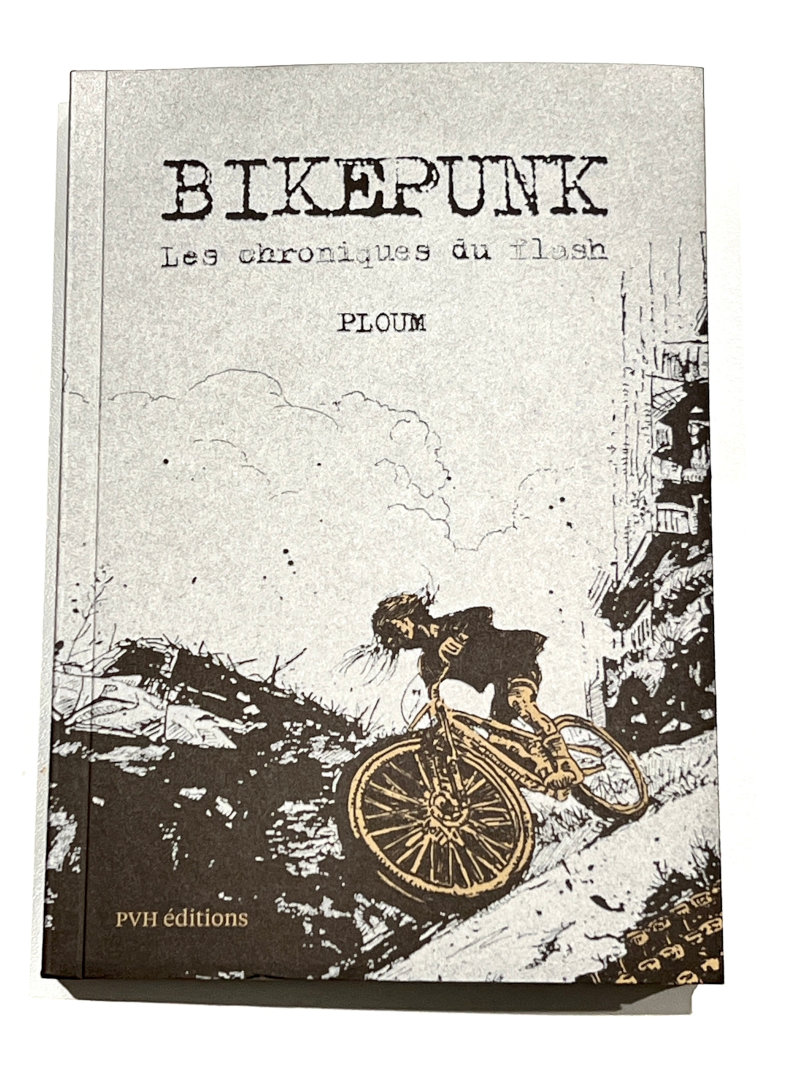 Couverture du livre Bikepunk : une cycliste en papier recyclé dévale une pente dans une ville dévastée entièrement argentée.